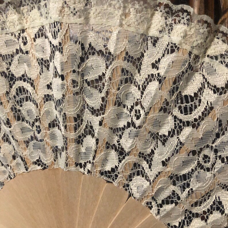 May include: A white lace fan with a wooden handle. The lace is delicate and intricate, with a floral pattern.