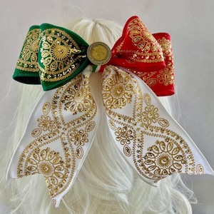May include: A large hair bow featuring a green section on the left and a red section on the right, both adorned with gold glitter floral patterns. The bottom consists of two white ribbon tails with gold glitter designs and a central coin accent.