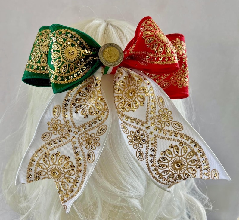 May include: A large hair bow featuring a green section on the left and a red section on the right, both adorned with gold glitter floral patterns. The bottom consists of two white ribbon tails with gold glitter designs and a central coin accent.
