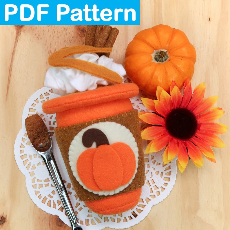 May include: A felt craft pattern for a pumpkin spice latte. The pattern includes a brown cup with a white lid, a swirl of whipped cream, a sprinkle of cinnamon, and a pumpkin on the side. The pattern also includes a small pumpkin and a sunflower.