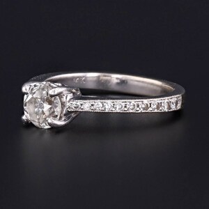 Puede incluir: Un anillo de compromiso de plata con un solo diamante redondo engastado en garras. La banda est&aacute; adornada con una fila de diamantes m&aacute;s peque&ntilde;os.