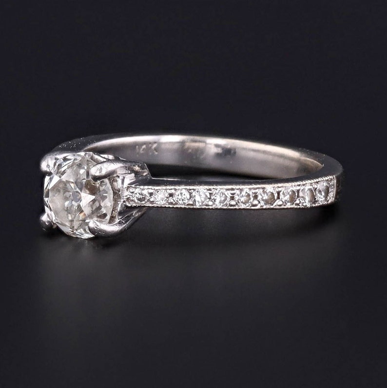 Puede incluir: Un anillo de compromiso de plata con un solo diamante redondo engastado en garras. La banda est&aacute; adornada con una fila de diamantes m&aacute;s peque&ntilde;os.
