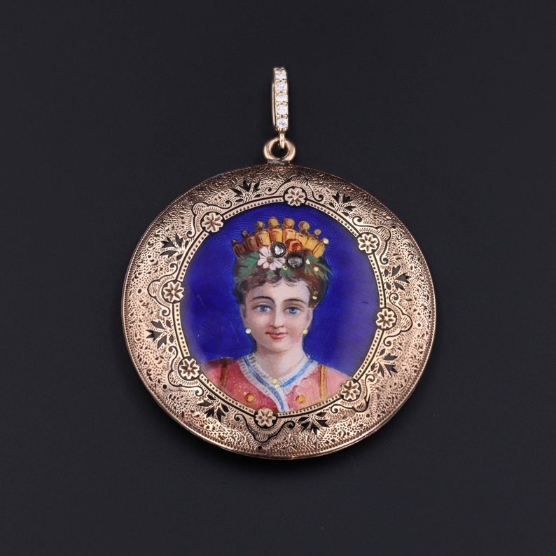 Pu&ograve; includere: Un ciondolo a medaglione in oro con un designo filigranato dettagliato. Il medaglione presenta un ritratto dipinto di una donna che indossa una corona e un abito rosa e oro. Lo sfondo del ritratto &egrave; di un blu profondo.