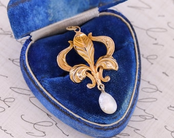 May include: A gold pendant with a pearl drop, in the shape of a stylized fleur-de-lis, in a blue velvet jewelry box.