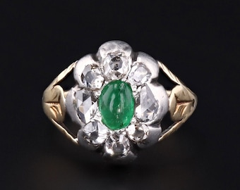 May include: A silver ring featuring a green emerald gemstone surrounded by smaller diamonds. The ring has a gold band.