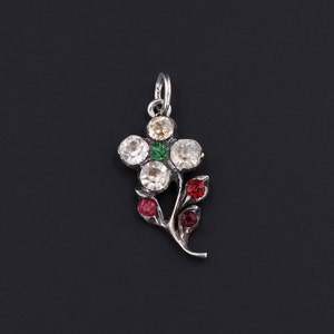 Puede incluir: Encanto de flor de plata con diamantes de imitación blancos, verdes y rojos. La flor tiene cinco pétalos y un tallo con hojas.