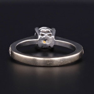 Puede incluir: Un anillo de compromiso de plata con un diamante redondo engastado en garras. La banda es lisa y tiene un peque&ntilde;o diamante a cada lado de la piedra central.