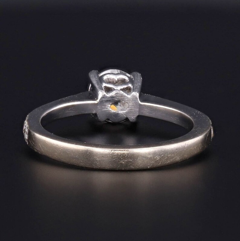 Puede incluir: Un anillo de compromiso de plata con un diamante redondo engastado en garras. La banda es lisa y tiene un peque&ntilde;o diamante a cada lado de la piedra central.
