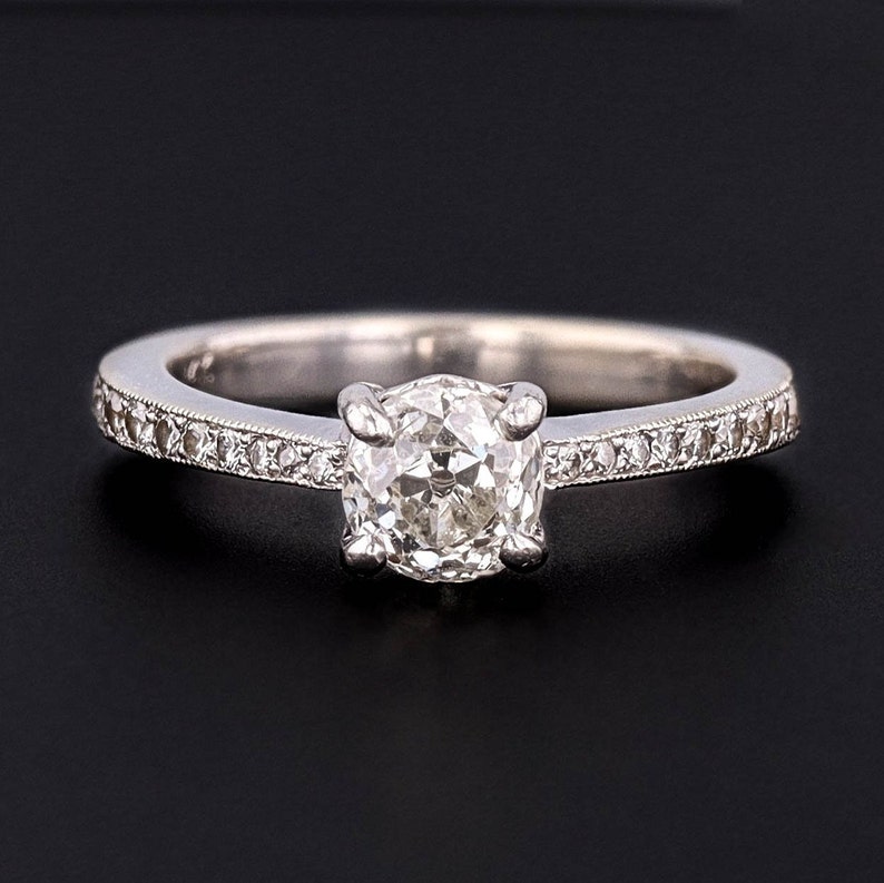 Puede incluir: Un anillo de plata con un solo diamante redondo engastado en una garra de cuatro puntas. La banda est&aacute; adornada con una fila de diamantes m&aacute;s peque&ntilde;os.