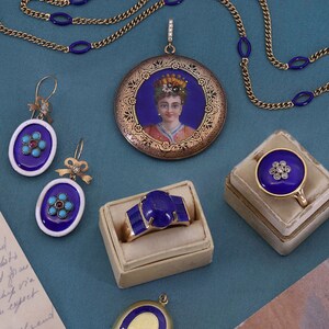 Pu&ograve; includere: Un set di gioielli con un medaglione d'oro con un ritratto dipinto, un anello con una grande pietra blu e orecchini con pietre blu e rosse.