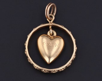 May include: Gold charm pendant featuring a heart-shaped charm hanging inside a circular frame with a decorative edge. The heart charm has the inscription "1-28-48" on the back.