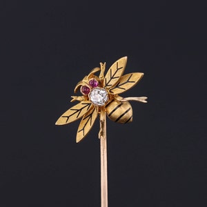 Op de afbeelding: Een gouden bij broche met diamant- en robijnaccenten. De bij zit op een gouden speld.