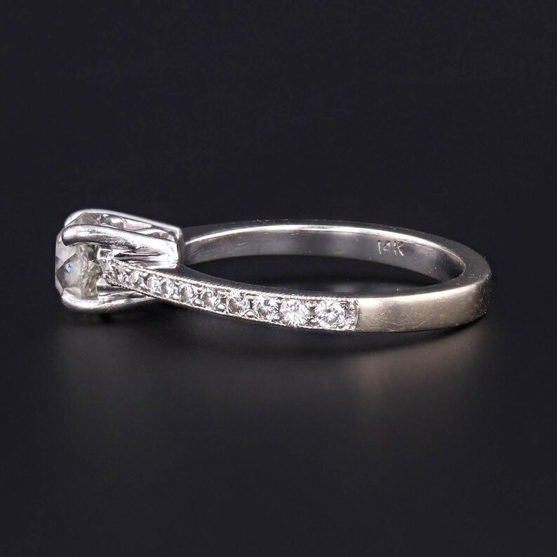 Puede incluir: Un anillo de plata con un solo diamante redondo y una banda de diamantes m&aacute;s peque&ntilde;os engastados en pav&eacute;. El anillo est&aacute; marcado con "14K" en el interior de la banda.