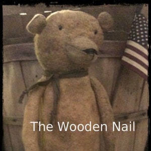 May include: A vintage-style, tan-colored teddy bear with a black ribbon around its neck. The bear is standing on a red platform with the text "The Wooden Nail" visible in the background.