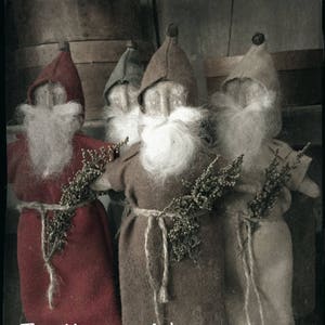 May include: Four handmade felt figures dressed as gnomes with long white beards and brown, red, and green felt hats. The figures are holding sprigs of greenery and are standing in front of a wooden background. The text "The Wooden Nail" is printed at the bottom of the image.