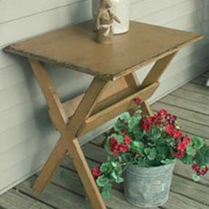May include: A small wooden table with a distressed brown finish and a shelf underneath. The table is standing on a wooden deck.