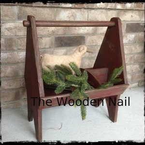 May include: A red wooden carrying rack with a handle, featuring a small stuffed lamb and a sprig of greenery. The rack is labeled "The Wooden Nail".