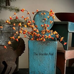 May include: A teal blue wooden planter with the text "The Wooden Nail" on the front. The planter is filled with a sprig of orange and red berries.