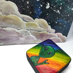May include: A small wooden box with a rainbow background and a green alien with big eyes painted on the lid.