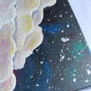 May include: A close-up of a small canvas painting with white textured clouds against a dark blue background with white splatter paint.