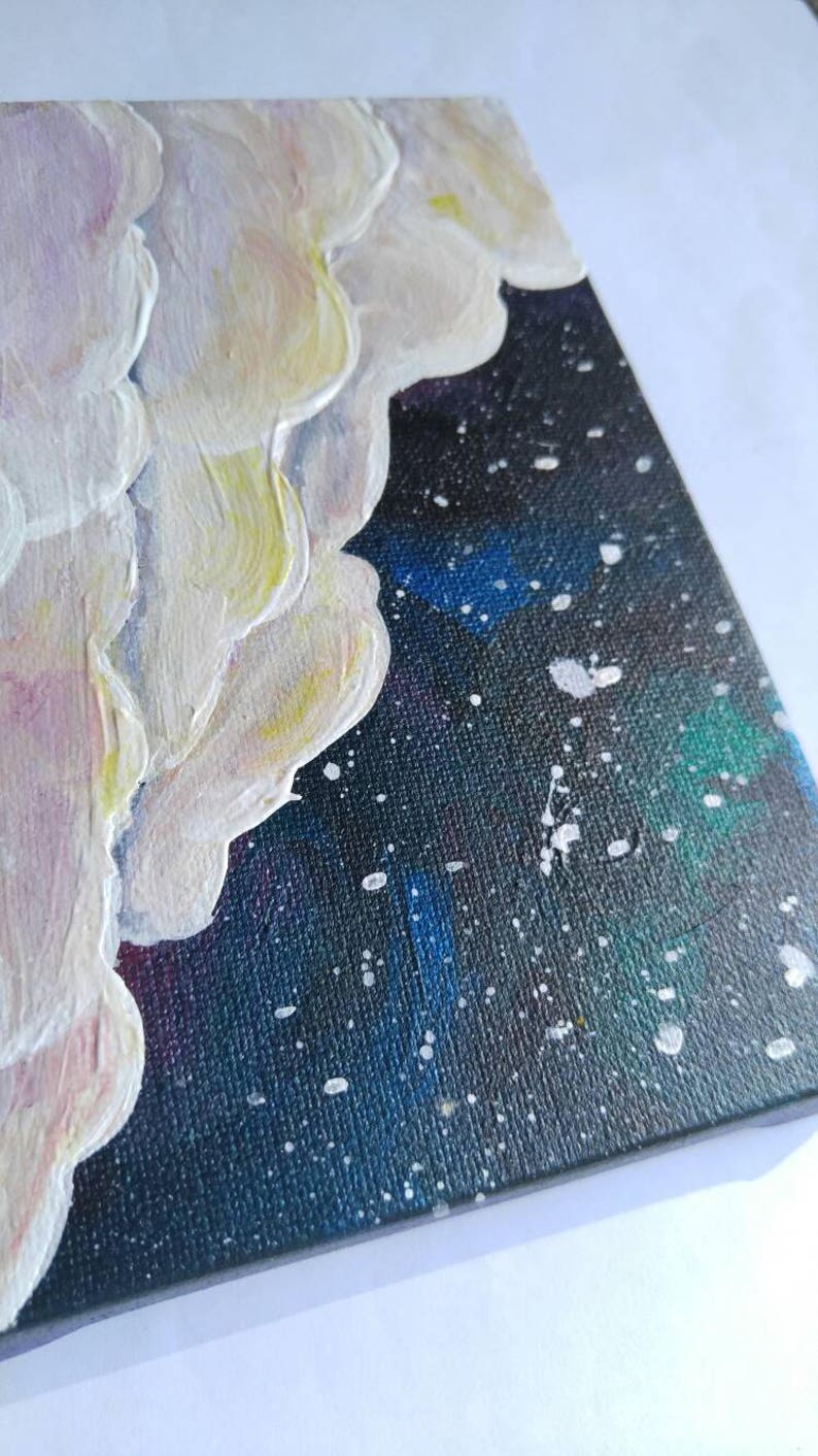 May include: A close-up of a small canvas painting with white textured clouds against a dark blue background with white splatter paint.