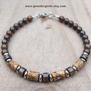 May include: A brown and beige beaded bracelet with silver accents. The bracelet is made with round and rectangular beads.
