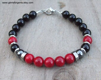 May include: A black and red beaded bracelet with a silver clasp. The bracelet features black onyx, red coral, and hematite beads.
