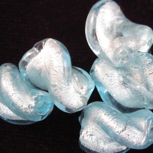 May include: Several light blue glass beads with a silver foil effect are arranged against a black background. The beads have a twisted, organic shape, and the silver foil adds a reflective quality to the translucent glass.