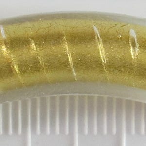 May include: A curved, clear glass bead with a gold foil interior and white vertical stripes. The bead has a cylindrical shape and is approximately 1 inch long.