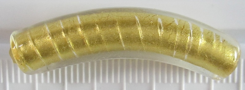 May include: A curved, clear glass bead with a gold foil interior and white vertical stripes. The bead has a cylindrical shape and is approximately 1 inch long.