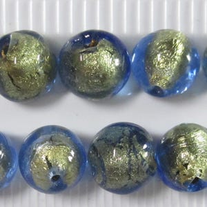 May include: Ten round glass beads with a blue and gold metallic design. The beads are arranged in two rows of five, showcasing a mix of blue and gold colors. These beads are suitable for jewelry making.