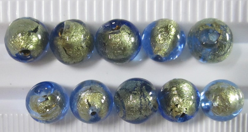 May include: Ten round glass beads with a blue and gold metallic design. The beads are arranged in two rows of five, showcasing a mix of blue and gold colors. These beads are suitable for jewelry making.