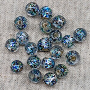 May include: A collection of clear glass beads with a speckled design. The beads feature a mix of blue, green, silver, and brown colors. Each bead has a hole running through the center, suggesting they are for jewelry making or crafts.