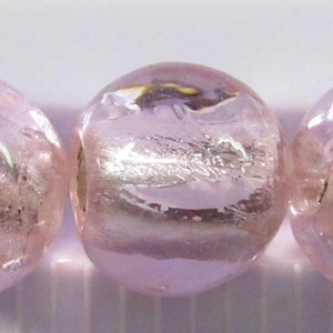 May include: Three round, light pink glass beads with a silver metallic stripe. The beads are translucent, allowing light to pass through. The beads are approximately 0.5 inches in diameter.