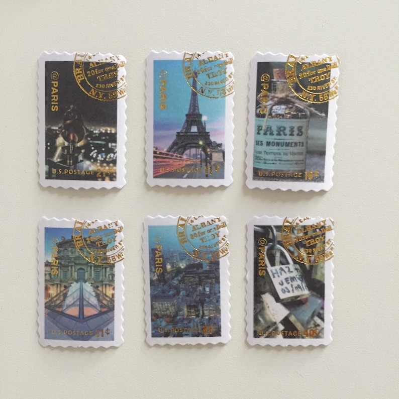 May include: Six postage stamps featuring images of Paris, France. Each stamp has a gold circular stamp with the text "ALBANY 20 for one roll TLDY NY 12205" and "@PARIS" printed on the stamp. The stamps feature images of the Eiffel Tower, a bridge, a building with a glass pyramid, a street scene, and a padlock on a bridge.
