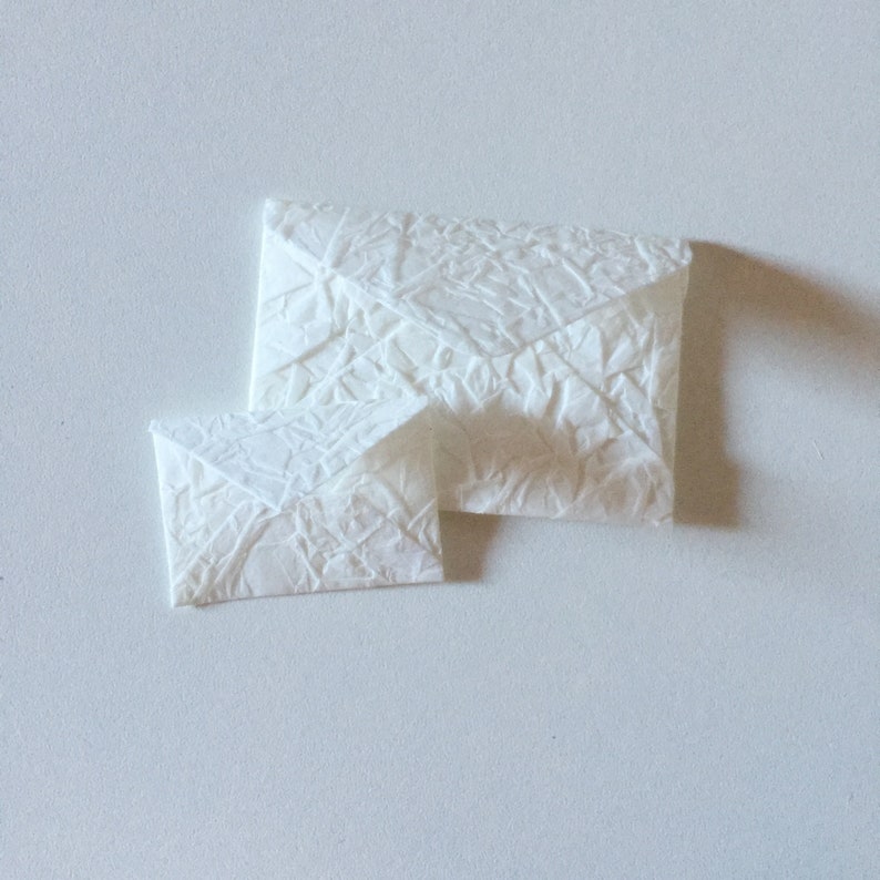 May include: Two white paper envelopes, one slightly larger than the other, with a textured surface. The envelopes are folded and ready to be used for sending letters or notes.