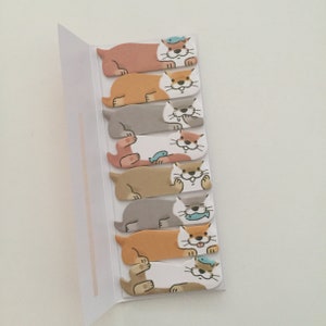 K&ouml;nnte beinhalten: Ein Satz von acht bunten Haftnotizen mit Comic-Ottern mit verschiedenen Gesichtsausdr&uuml;cken. Die Otter halten Fische und tragen H&uuml;te. Die Notizen sind an einer wei&szlig;en Karte befestigt.