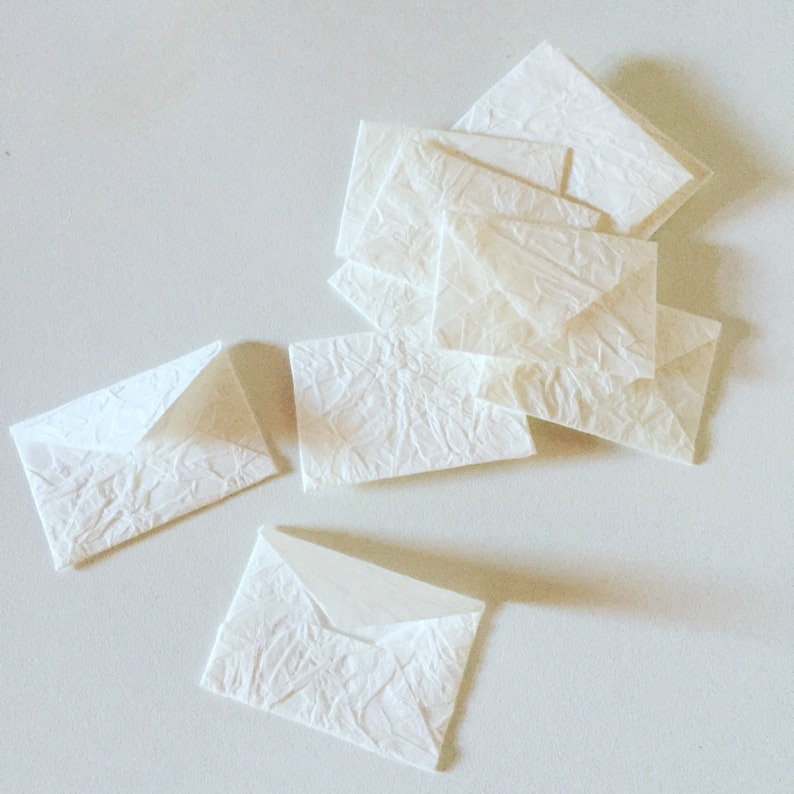May include: A stack of white, textured paper envelopes. The envelopes are folded and ready to be used for sending letters or notes.