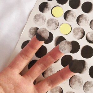 May include: A sheet of moon phase stickers with a variety of moon phases, including a full moon, crescent moon, and new moon. The stickers are black and white and have a matte finish.