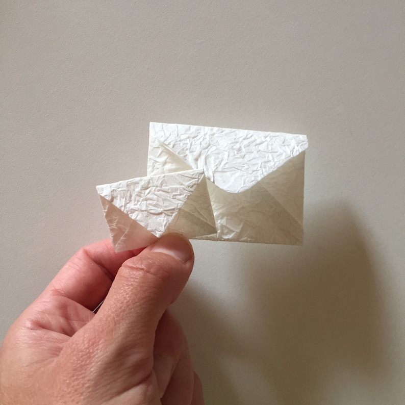 May include: Two white origami envelopes folded together. The envelopes are made of textured paper.