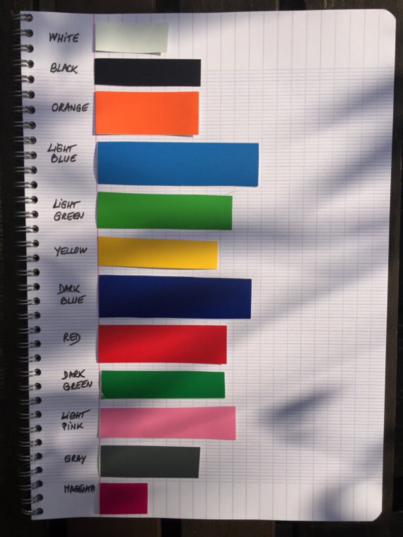 May include: A notebook page with color swatches labeled with the names of the colors: white, black, orange, light blue, light green, yellow, dark blue, red, dark green, light pink, gray, and magenta.