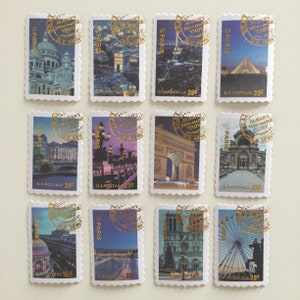 May include: Twelve vintage postage stamps featuring images of Paris, France. Each stamp has a gold foil design with the text "@PARIS" and "ALBANY 20 for TROY N.Y. 58" in a circle. The stamps feature various landmarks including the Eiffel Tower, Notre Dame Cathedral, and the Arc de Triomphe.