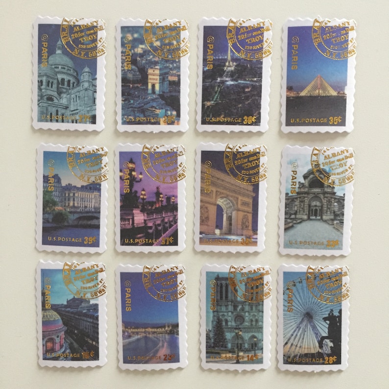 May include: Twelve vintage postage stamps featuring images of Paris, France. Each stamp has a gold foil design with the text "@PARIS" and "ALBANY 20 for TROY N.Y. 58" in a circle. The stamps feature various landmarks including the Eiffel Tower, Notre Dame Cathedral, and the Arc de Triomphe.