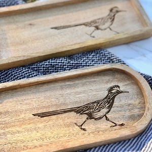 May include: Two wooden serving trays with a carved roadrunner design. The trays are made of light brown wood and have a natural finish.