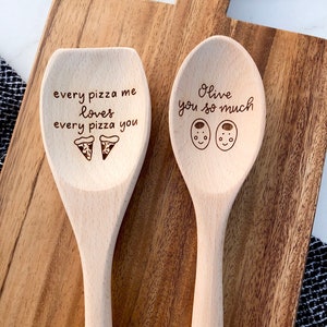 Two twelve inch beech wood utensils are engraved with food related puns. The spoon reads Olive you so much and includes two cute, smiling olives. The wooden spatula says every pizza me loves every pizza you and has two pizza icons engraved below