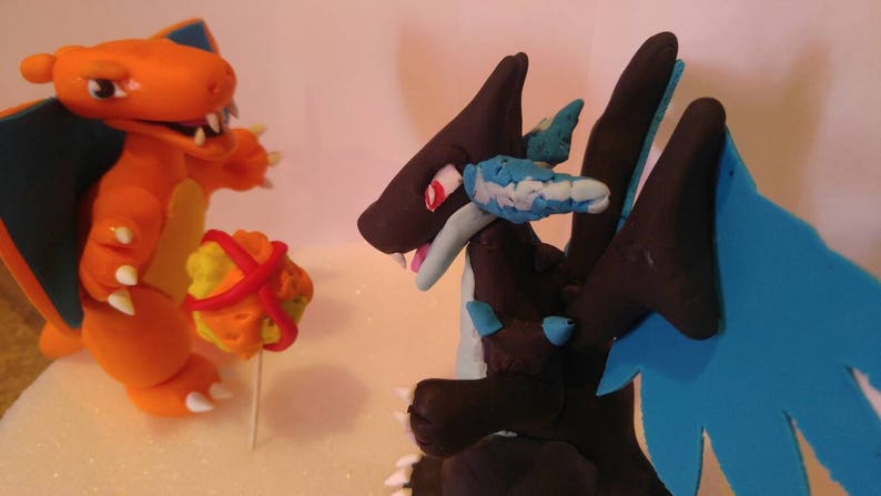 Puede incluir: Dos figuras de Pok&eacute;mon hechas a mano, Charizard y Dragonite, hechas de arcilla polim&eacute;rica. Charizard es naranja con la barriga amarilla y las alas azules. Dragonite es negro con alas azules y una parte inferior azul claro.