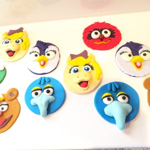 May include: A set of ten colorful cupcake toppers featuring characters from Sesame Street. The toppers are made of fondant and feature characters like Big Bird, Elmo, Cookie Monster, and Bert and Ernie.