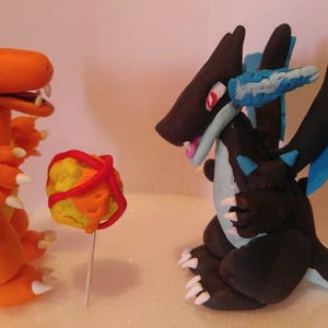 Puede incluir: Dos figuras de Pok&eacute;mon hechas a mano, un Dragonite negro y azul y un Charizard naranja, con una Pok&eacute; Ball roja, naranja y amarilla en el fondo.