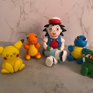May include: Five Pokemon figurines, including a trainer with a red shirt and blue jeans, a yellow Pikachu, a green Bulbasaur, a blue Squirtle, and an orange Charmander.