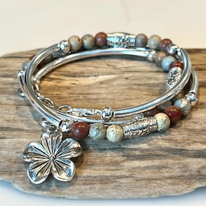 May include: A silver bracelet with a flower charm. The bracelet is made of multiple strands of silver beads and has a natural stone look.